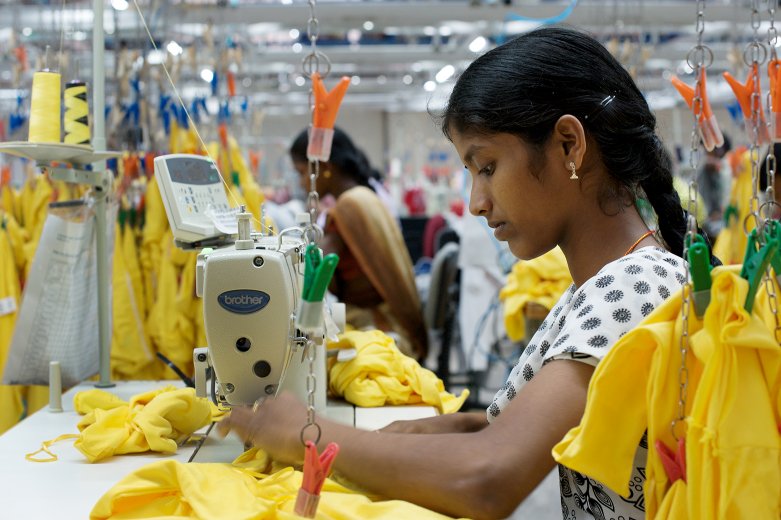 Young woman operating sewing machine in factory