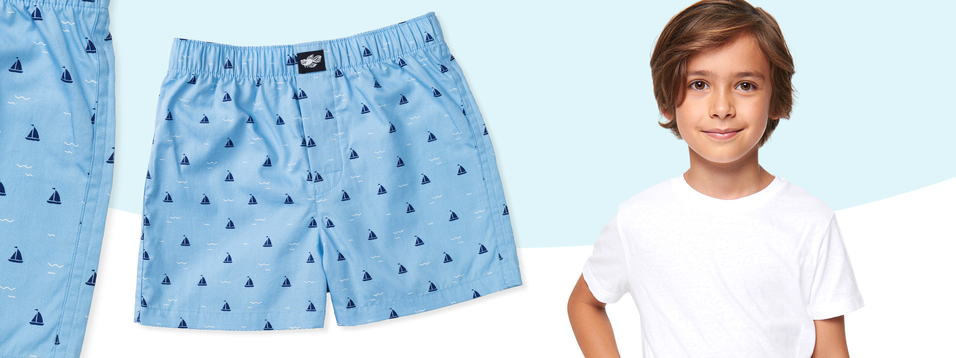 Light blue cotton boxer briefs with sailboat pattern and a boy wearing a white t-shirt on a light blue background